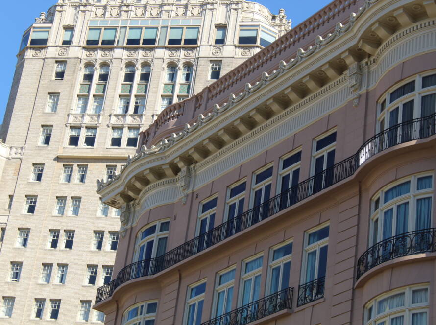 Two contrasting multi-story buildings — one ornate and pink, one tall and beige — symbolizing layered strategy and enduring SME growth.